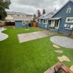 Blue house with a backyard featuring green turf and circular stone pavement.