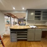 Newly finished kitchen with green cabinets and wood floors. Living room seen in the background.