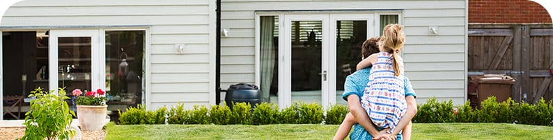 A father carrying his daughter on his back as they walk toward through their lawn toward their home.