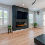 Living room with grey walls and inset fireplace. Large TV mounted above the fireplace.