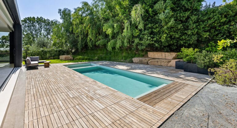 Modern renovated pool with a wooden deck and lush greenery, creating a peaceful ambiance