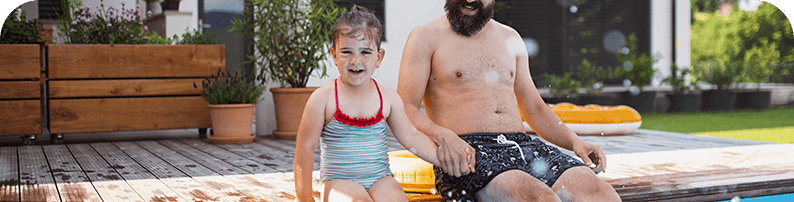 Happy father and her daughter sitting pleased on the wooden deck next to the pool
